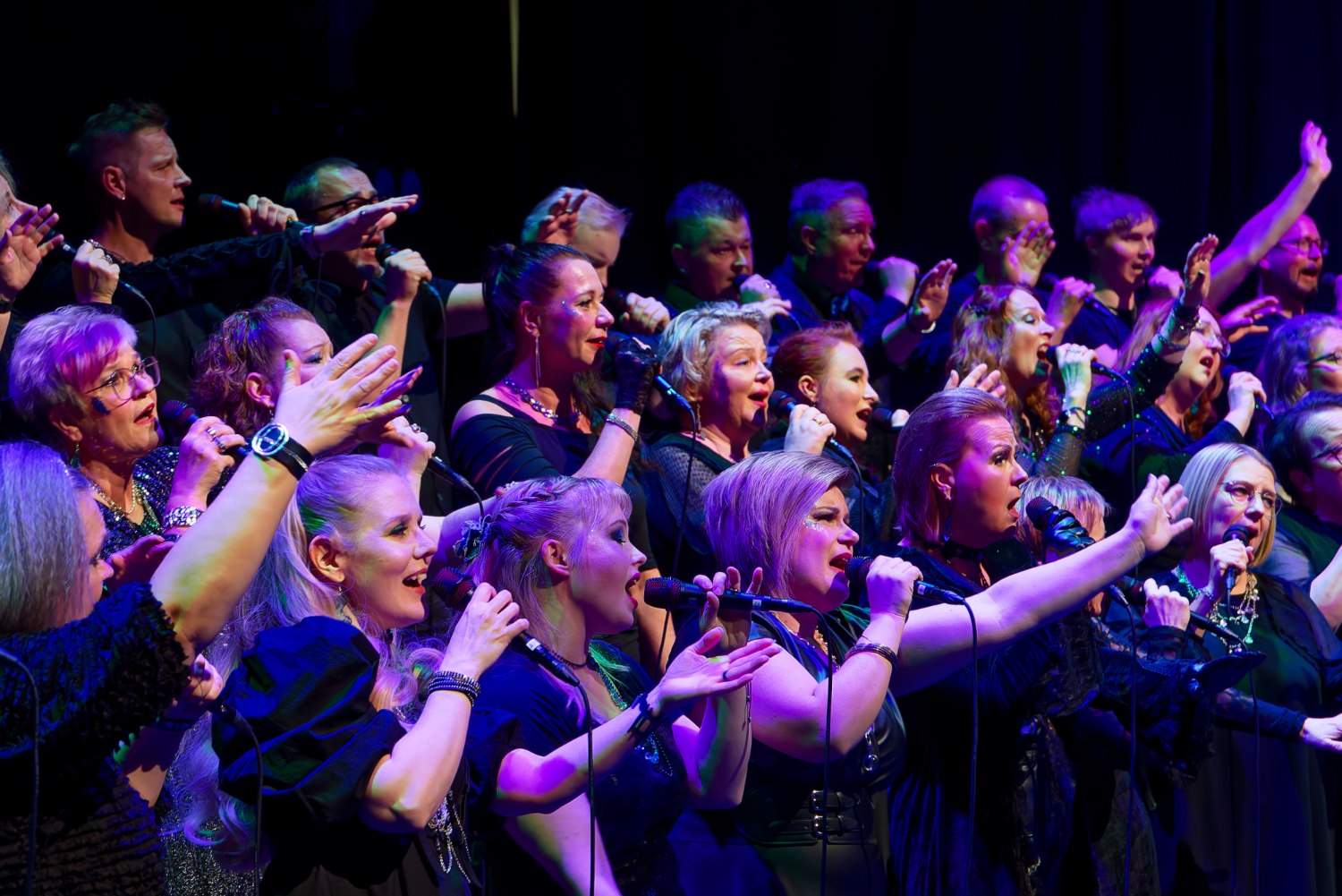 Kuorolaiset laulamassa lavalla kädet ojennettuna.