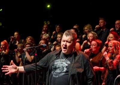 Miessolisti ja kuorolaiset esiintymässä lavalla punaisissa valoissa.