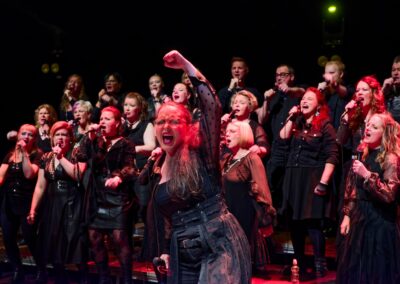 Solisti ja kuoro esiintymässä lavalla punaisissa valoissa.