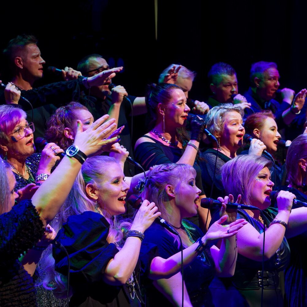 Kuorolaiset laulamassa lavalla kädet ojennettuna.