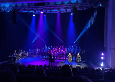 Kuoro ja kaksi solistia esiintymässä konsertissa sinisissä valoissa.